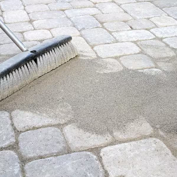 Broom sweeping sand onto stone pavers for outdoor cleaning and maintenance.