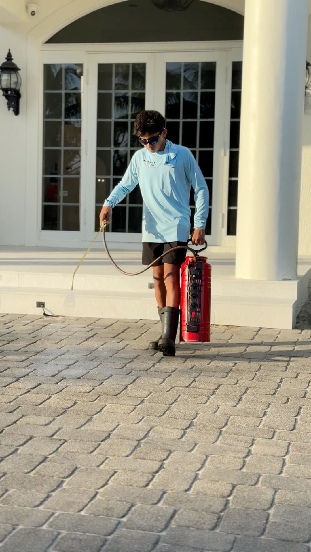 Person in a blue shirt uses a fire extinguisher on a stone pathway by a building.