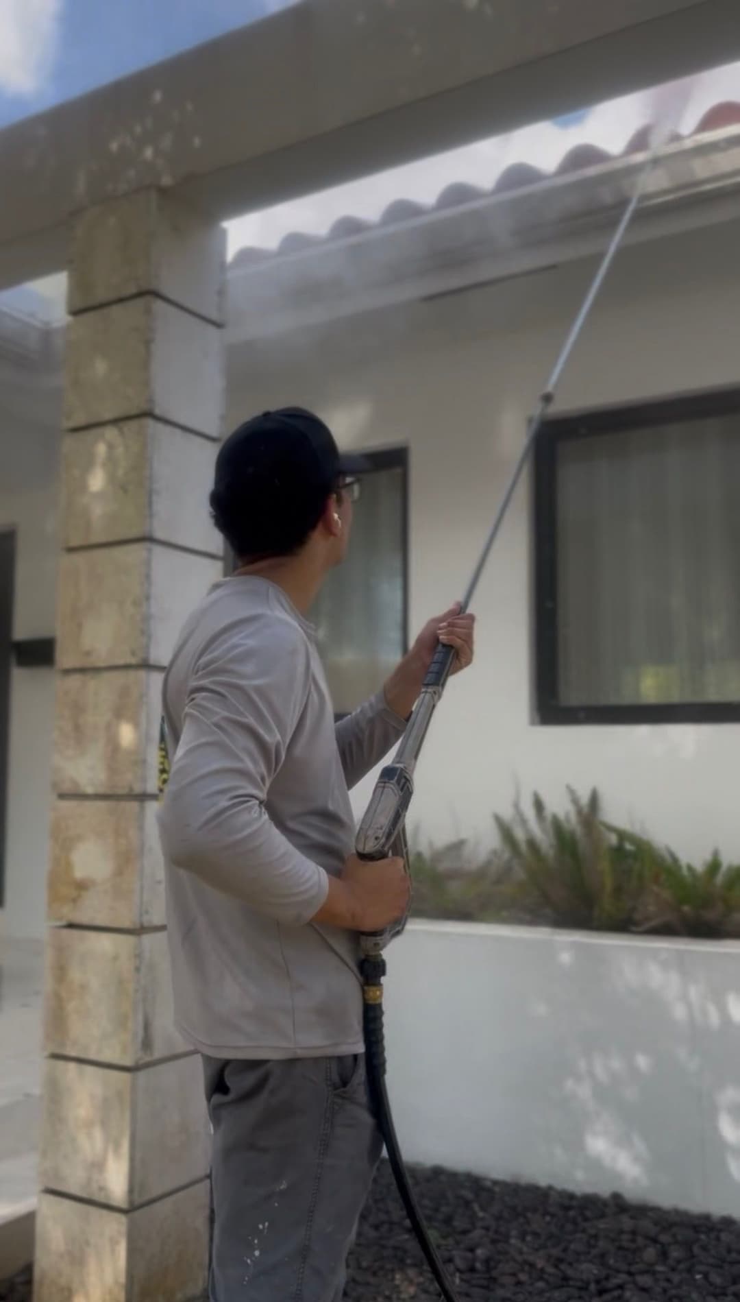 Man using a pressure washer to clean the exterior of a house. Sunlight shines above.