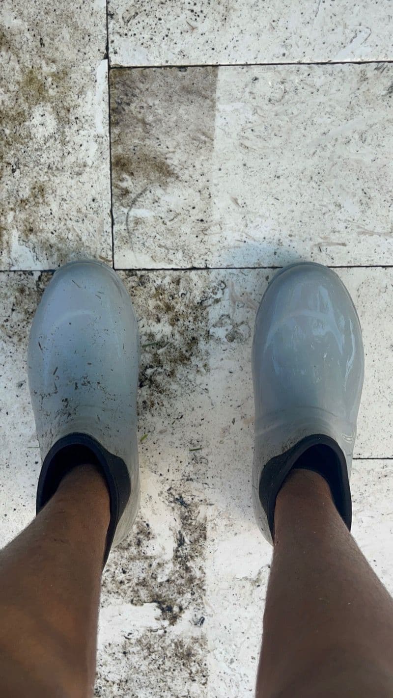 Dirty gray rubber boots on a tiled floor with visible stains and dirt.
