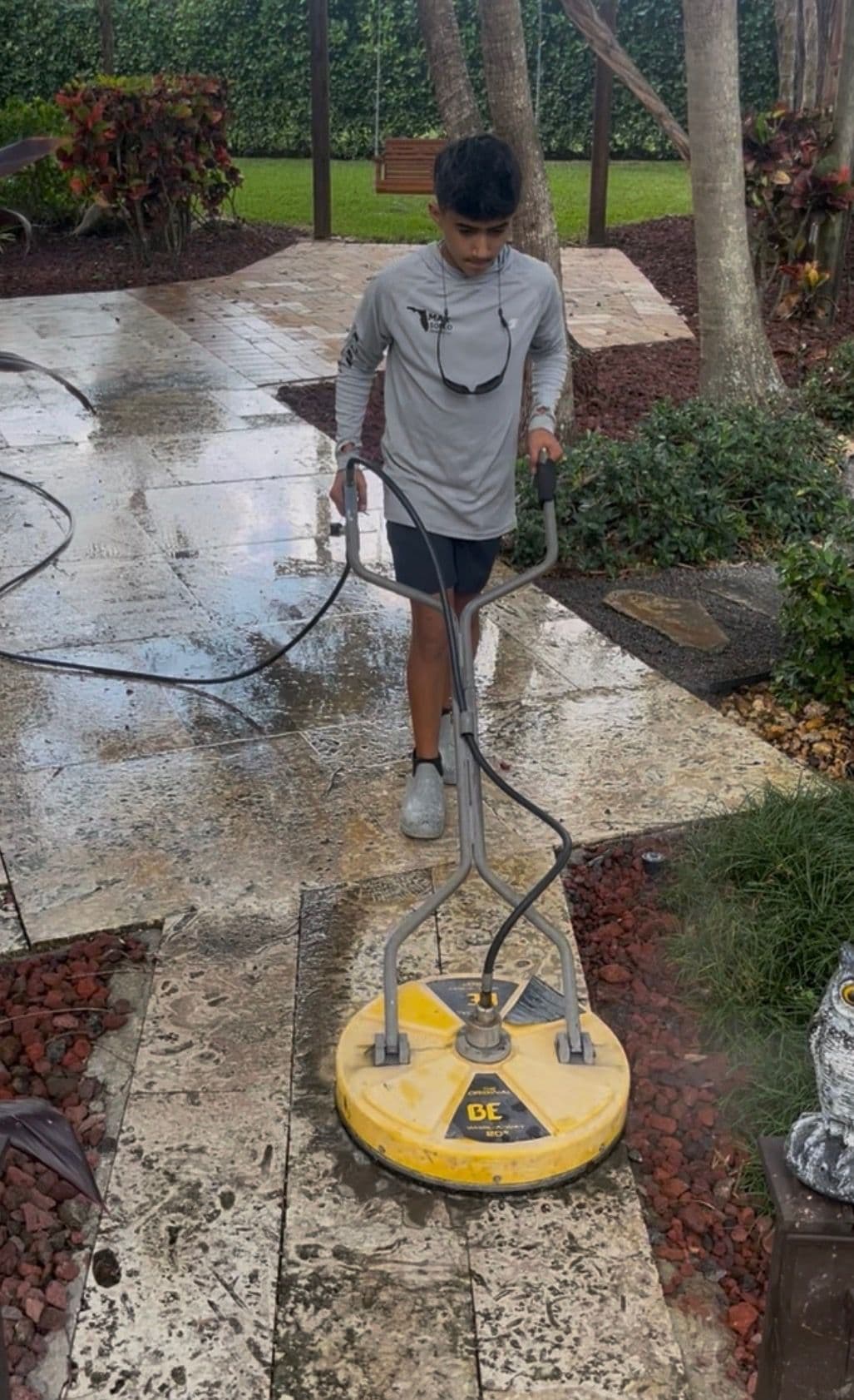 Youth washing patio with yellow surface cleaner, ensuring a spotless outdoor space.