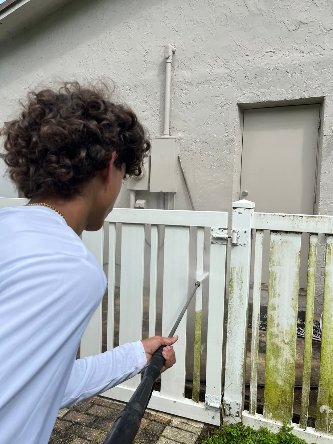 Teen pressure washing a fence to remove dirt and grime outside a home.
