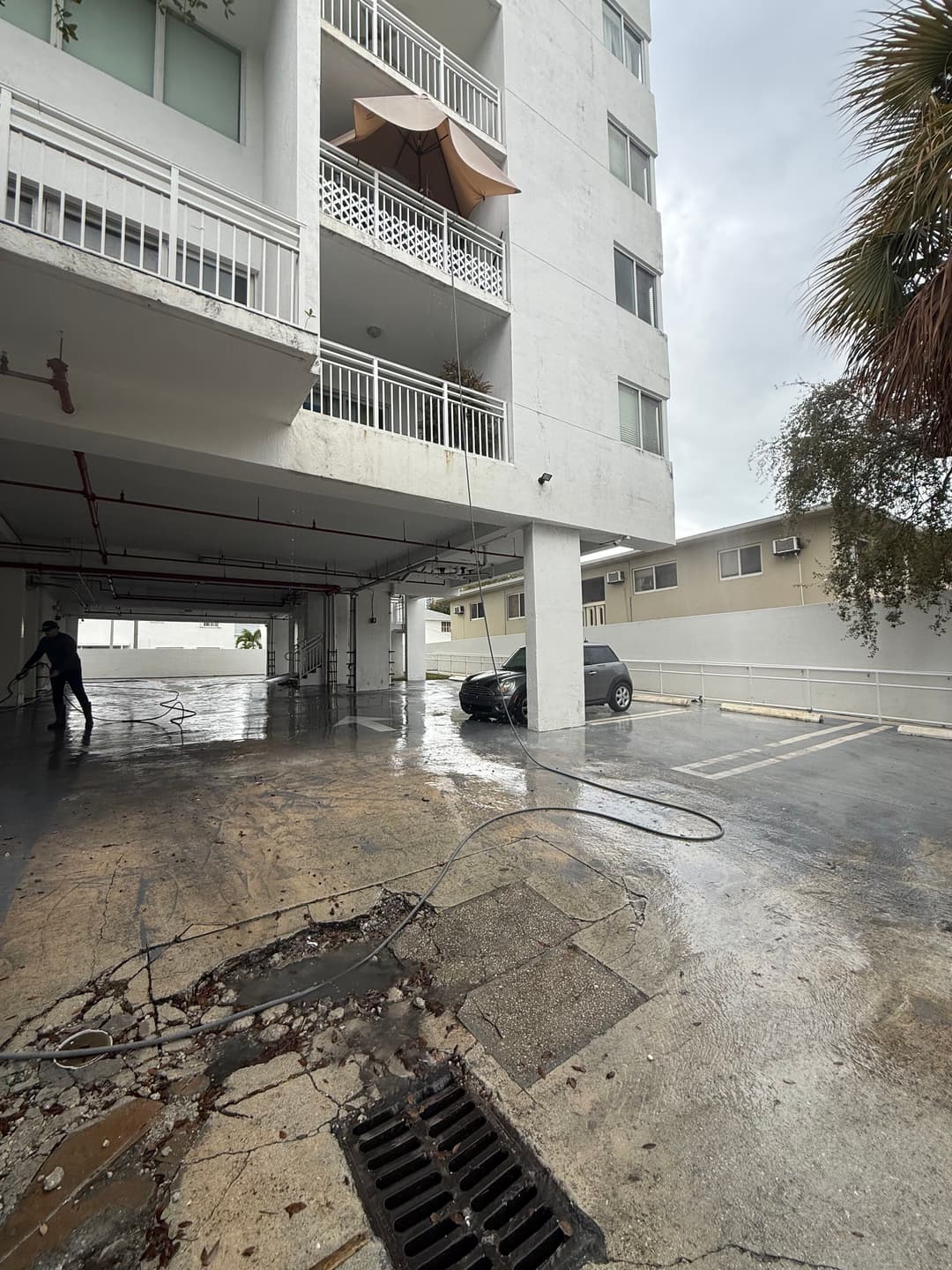 Wet parking garage with a car, power washing equipment, and a balcony with an umbrella.