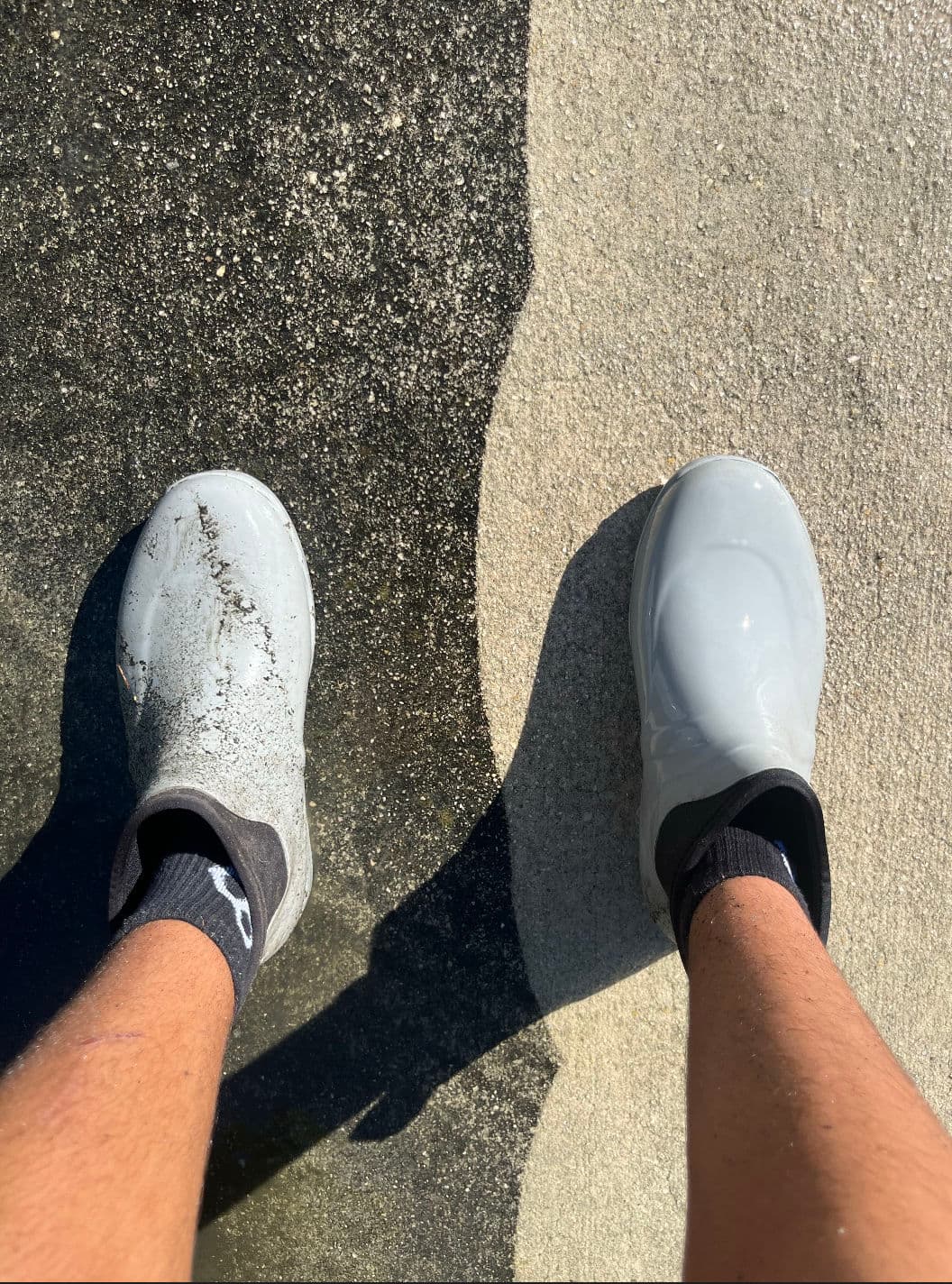 Person wearing gray clogs on a concrete surface, one shoe dirty and the other clean.