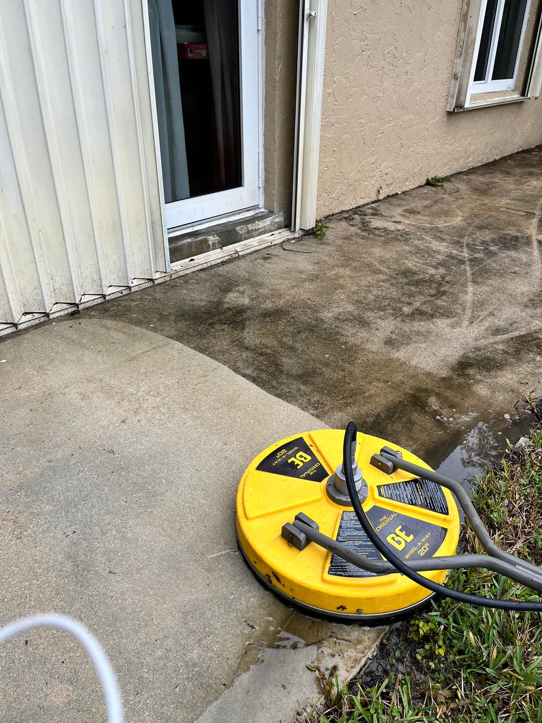 Pressure washer on concrete patio near sliding door, showing recent cleaning efforts.
