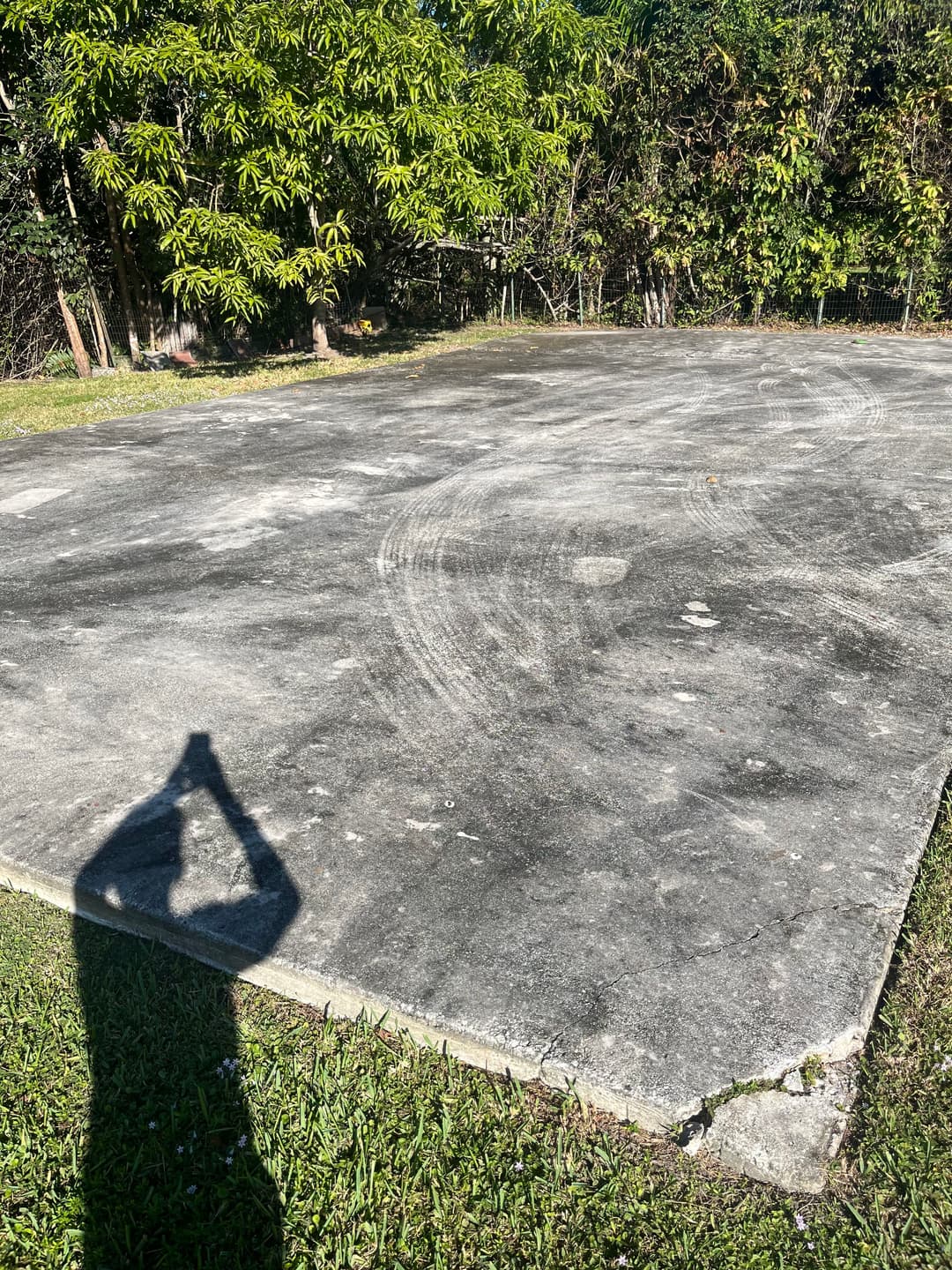 Concrete slab in a grassy area surrounded by trees, with a shadow in the foreground.